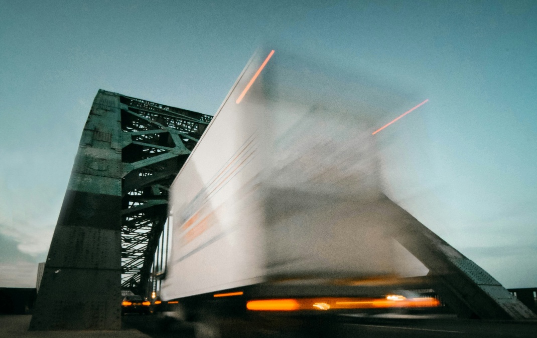 Blurred truck crossing a steel bridge at dusk, captured with motion blur.