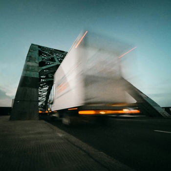 Blurred truck crossing a steel bridge at dusk, captured with motion blur.